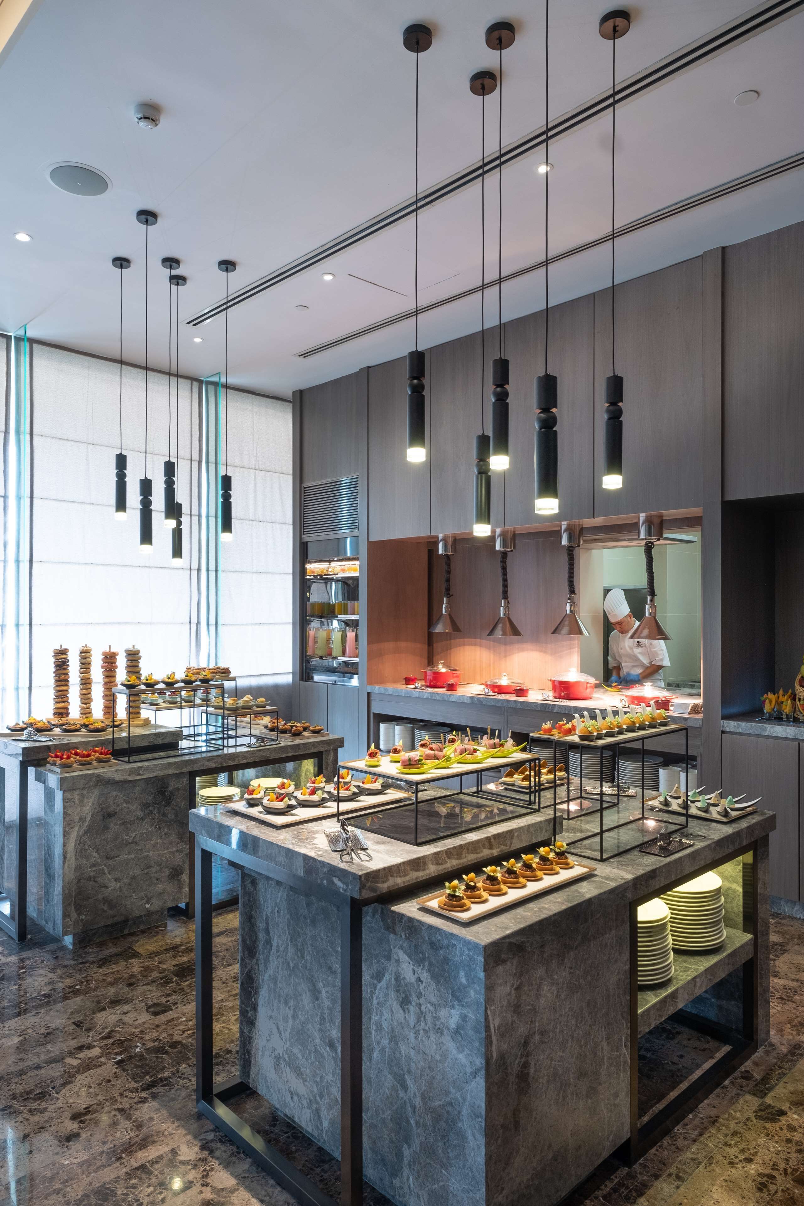 Une cuisine moderne avec des plans de travail en marbre, des luminaires suspendus et un chef qui prépare les plats.