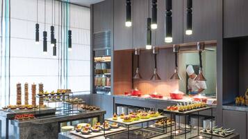 Une cuisine moderne avec des plans de travail en marbre, des luminaires suspendus et un chef qui prépare les plats.