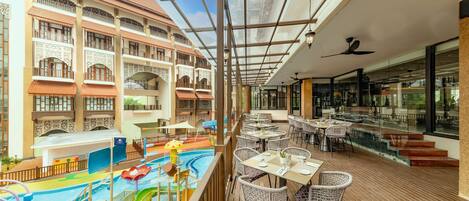 A deck with tables and chairs, a pool area, and a building with balconies.