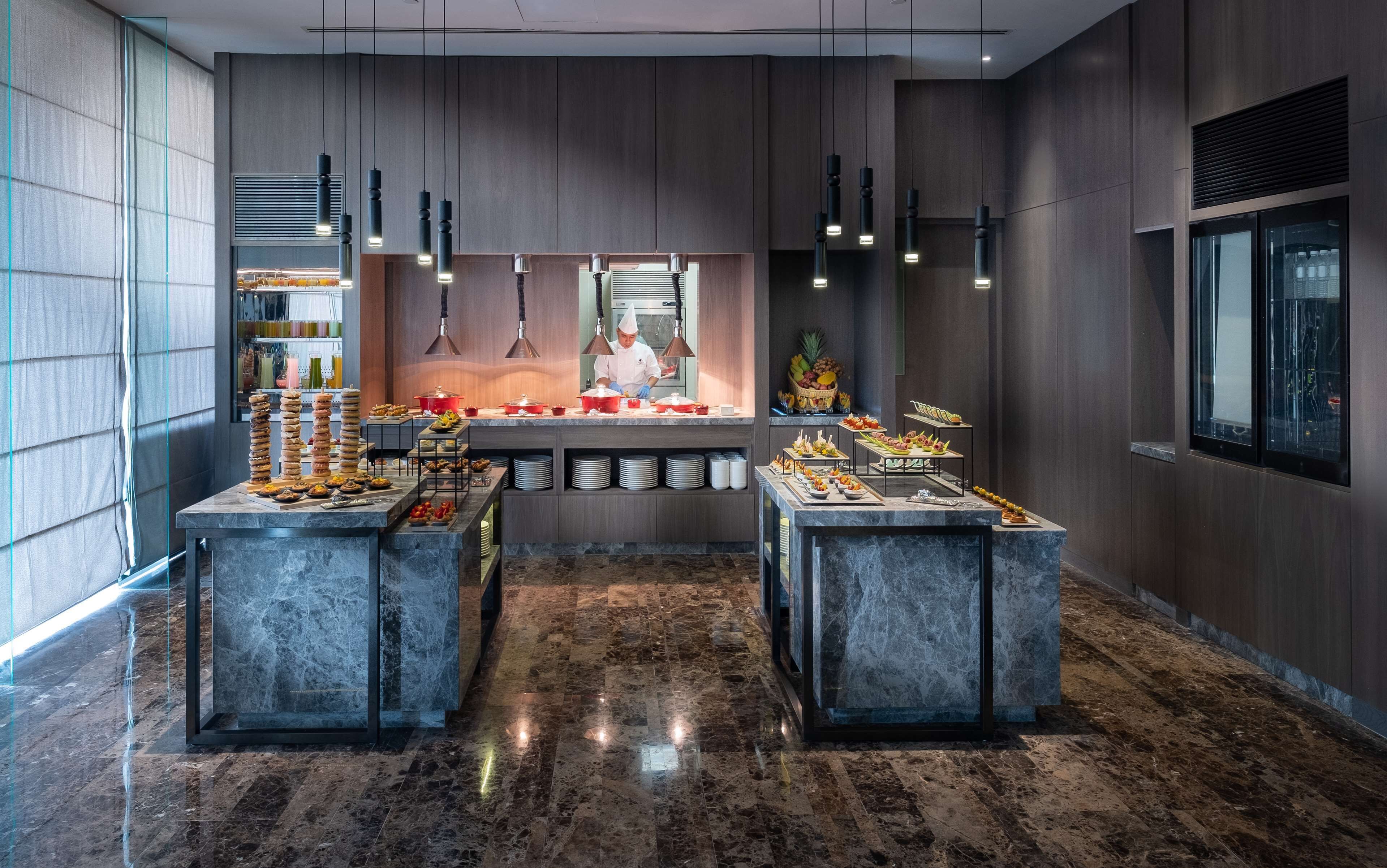 Un hall d’hôtel moderne avec un sol en marbre, un buffet et un chef qui prépare les plats.