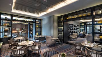 Un ristorante moderno con diverse aree dedicate alla ristorazione, tra cui tavoli rotondi e sgabelli alti, e una cucina a vista.