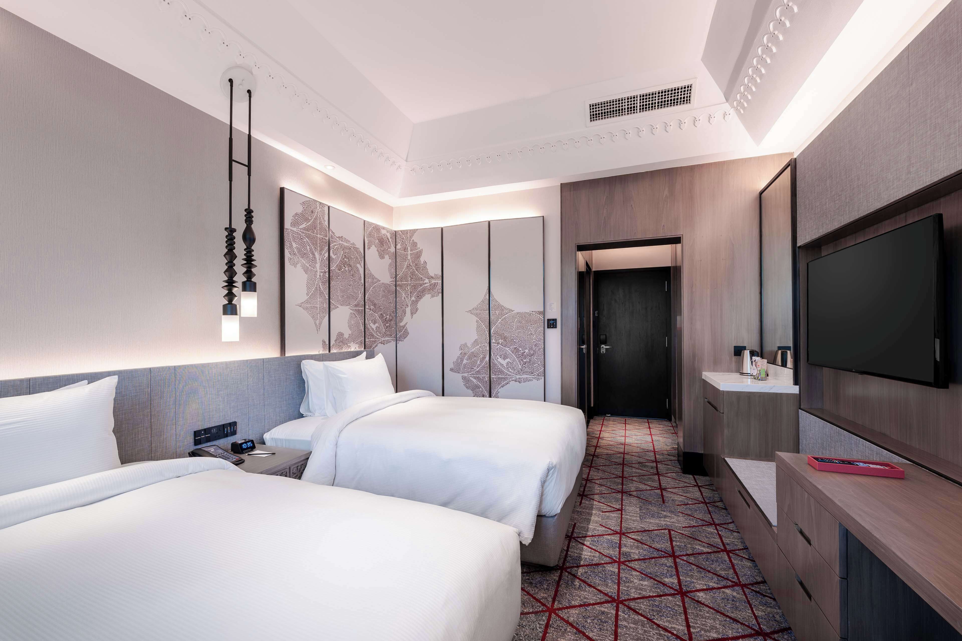 Quarto de hotel com duas camas, televisão, escrivaninha e carpete estampado.