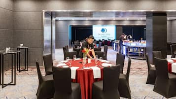 A conference room with round tables, black chairs, and a red tablecloth. A banner with "DOUBLETREE by Hilton" is visible in the background.