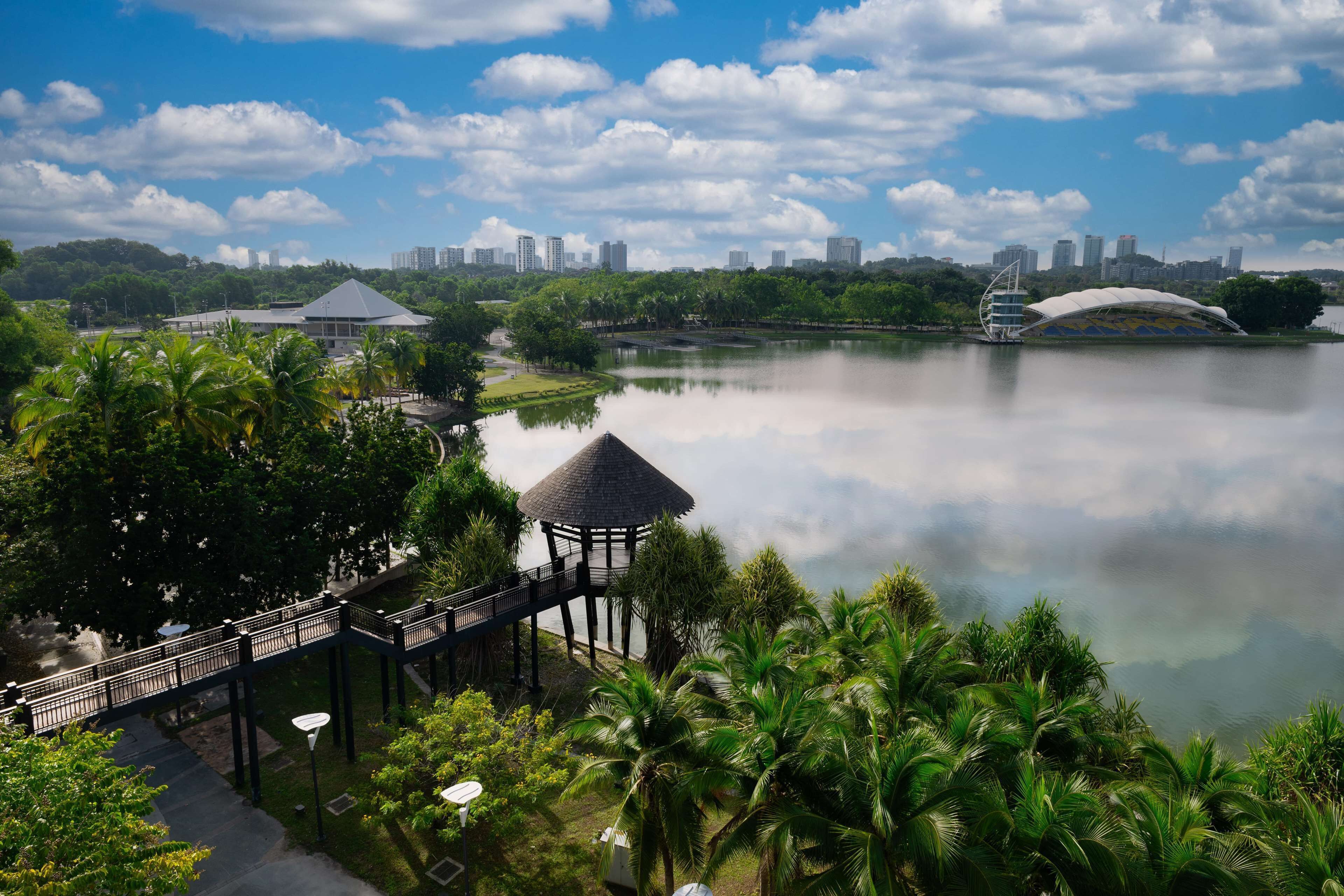 A park with a bridge, a gazebo, and a lake reflecting buildings.