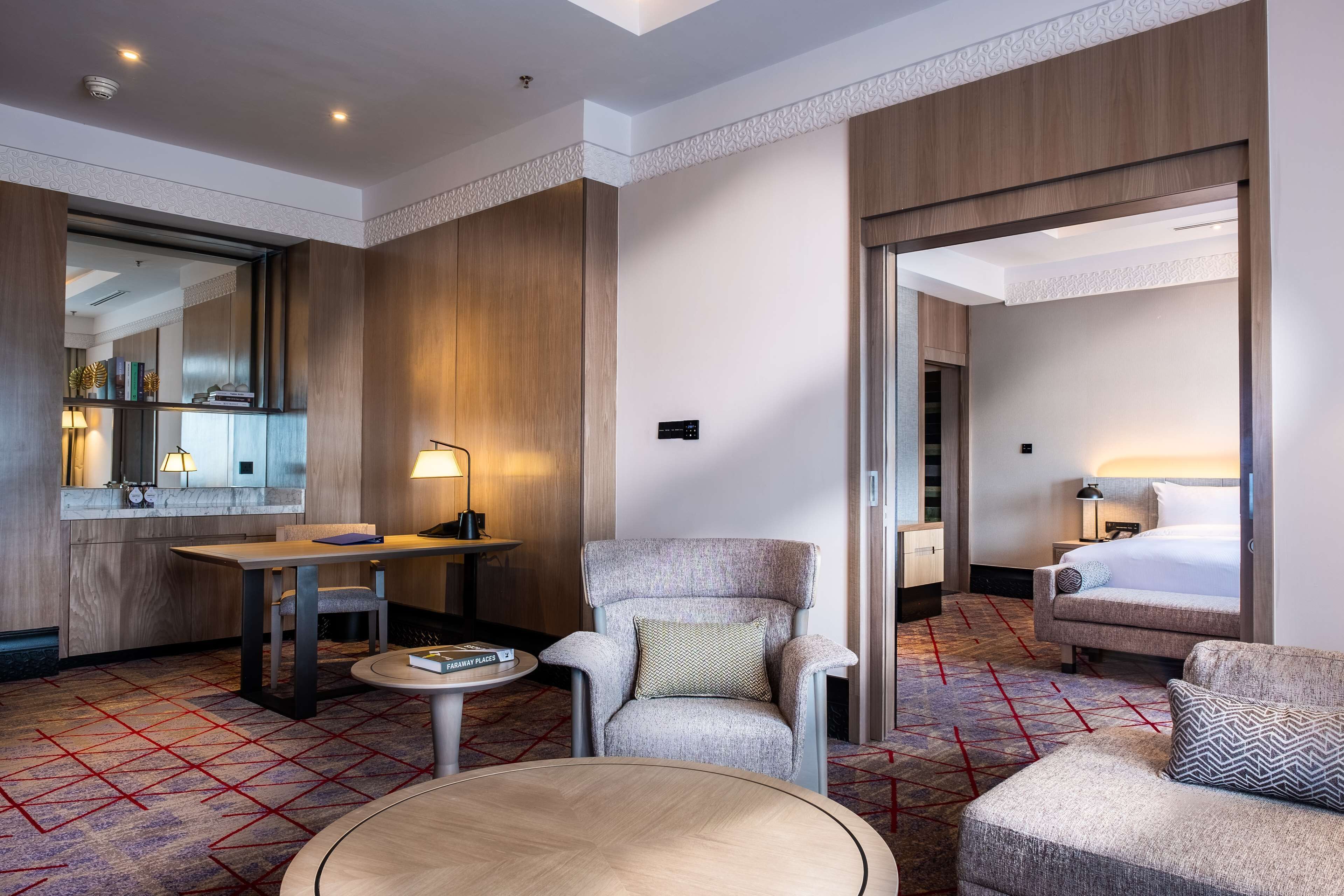 Ein Hotelzimmer mit einer Wand in Holzoptik, einem runden Tisch, einem bequemen Sessel, einer Couch und einem Bett.