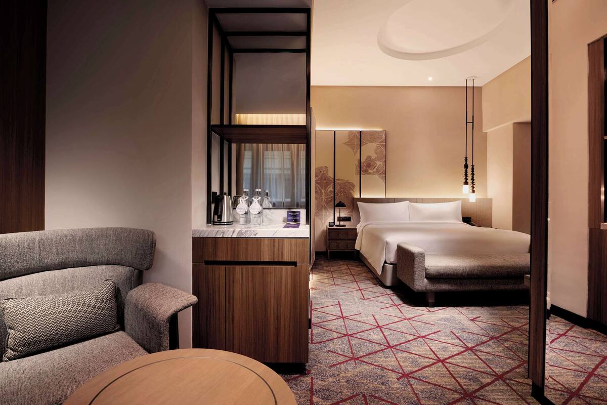 A hotel room with a sofa, a small table, a bed, a nightstand, and a mirror.