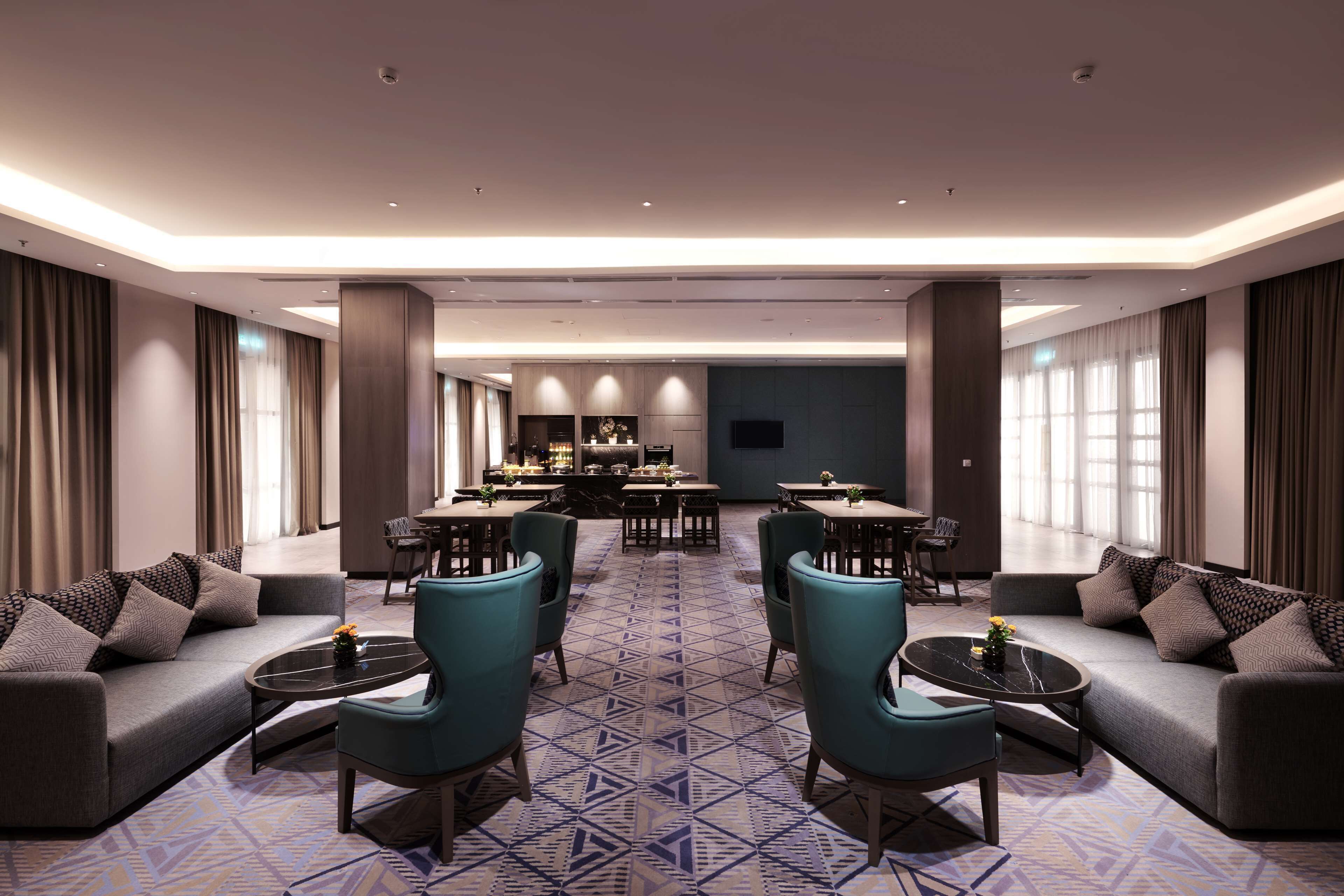A modern hotel lobby with a central dining area, sofas, and a patterned floor.