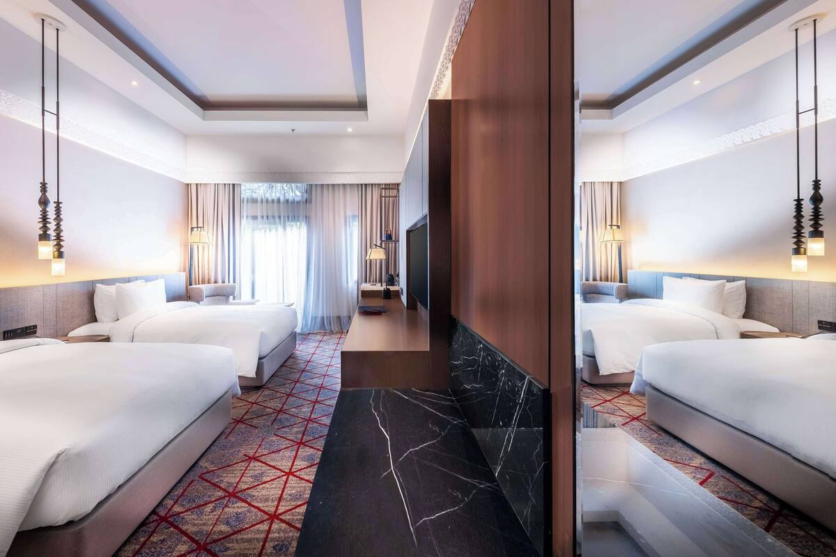 A hotel room with two beds, a TV, a desk, and a bathroom.