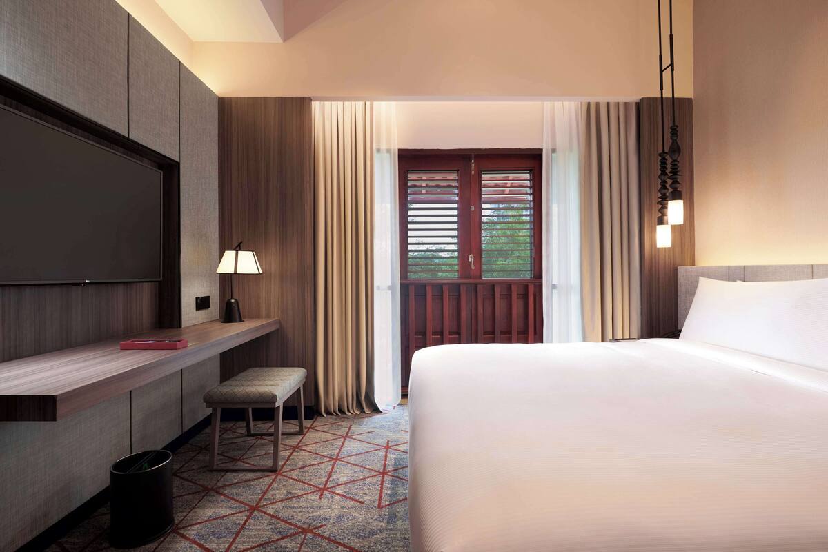 A hotel room with a large bed, a desk with a chair, a TV, and a window with curtains.