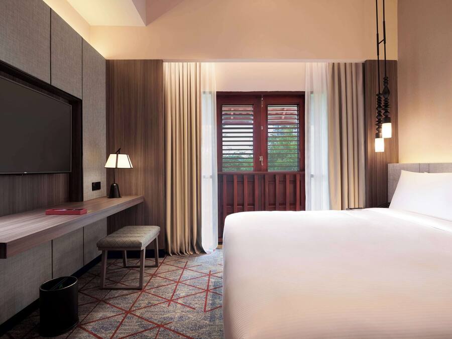 A hotel room with a large bed, a desk with a chair, a TV, and a window with curtains.