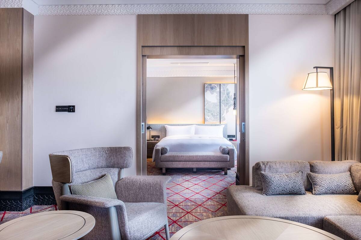 A hotel room with a bed, two armchairs, a sofa, a small table, and a lamp.
