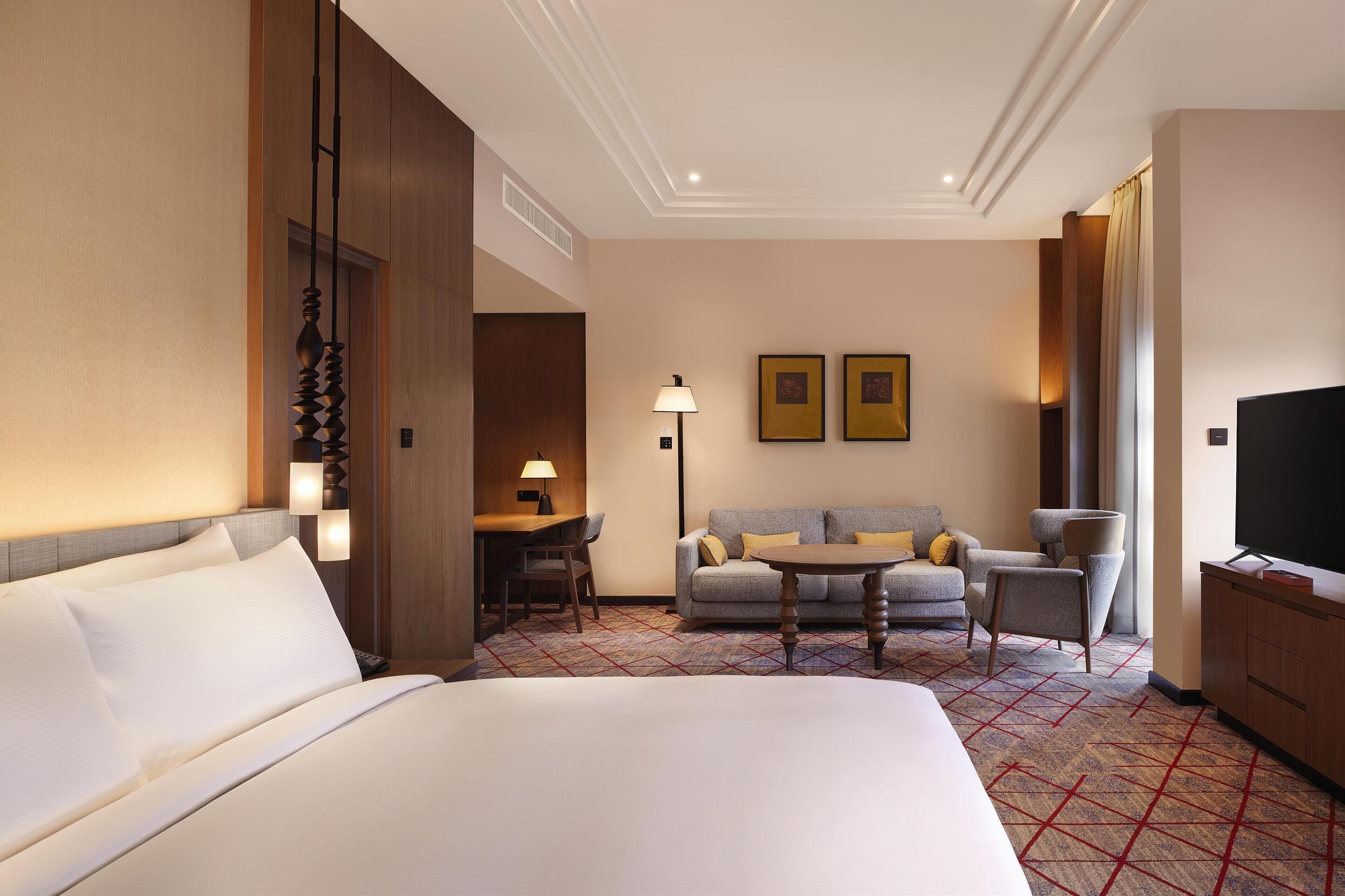 Ein Hotelzimmer mit einem großen Bett, einer Sitzecke, einem kleinen Tisch und einem Fernseher.