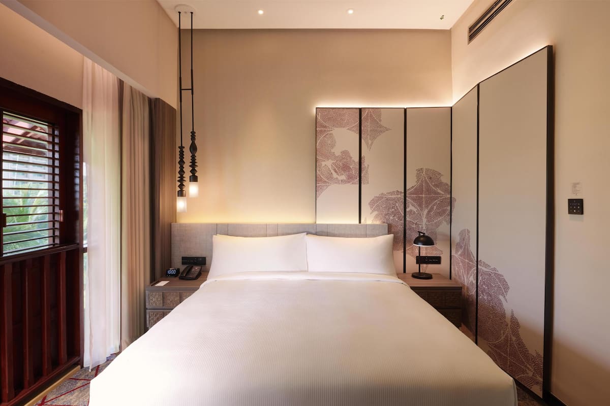 A neatly made bed with a headboard, bedside tables with lamps, a phone, and a wall with a leaf pattern.