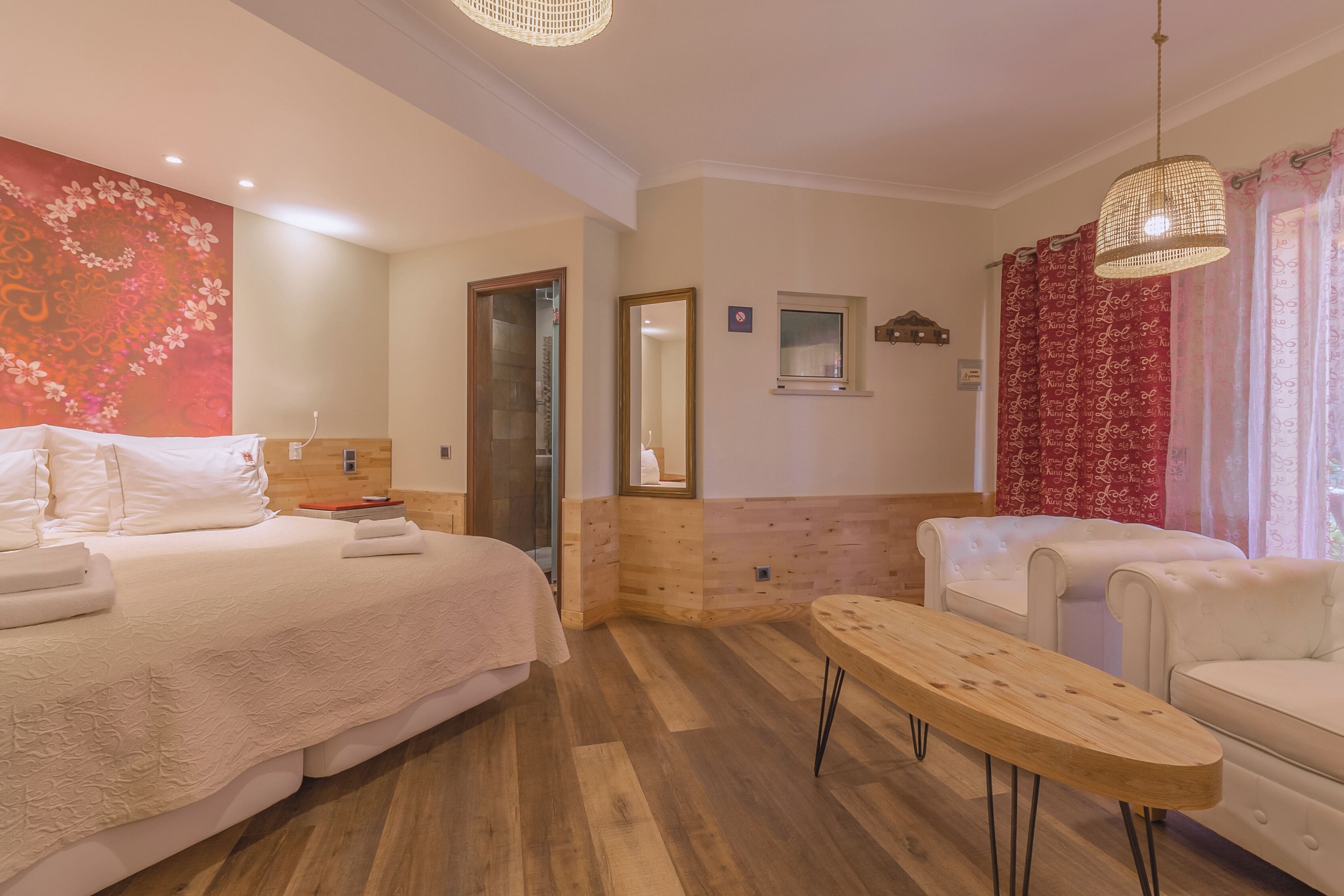 Una habitación de hotel con cama, una mesa de madera, sofá, espejo y ventana con cortinas.