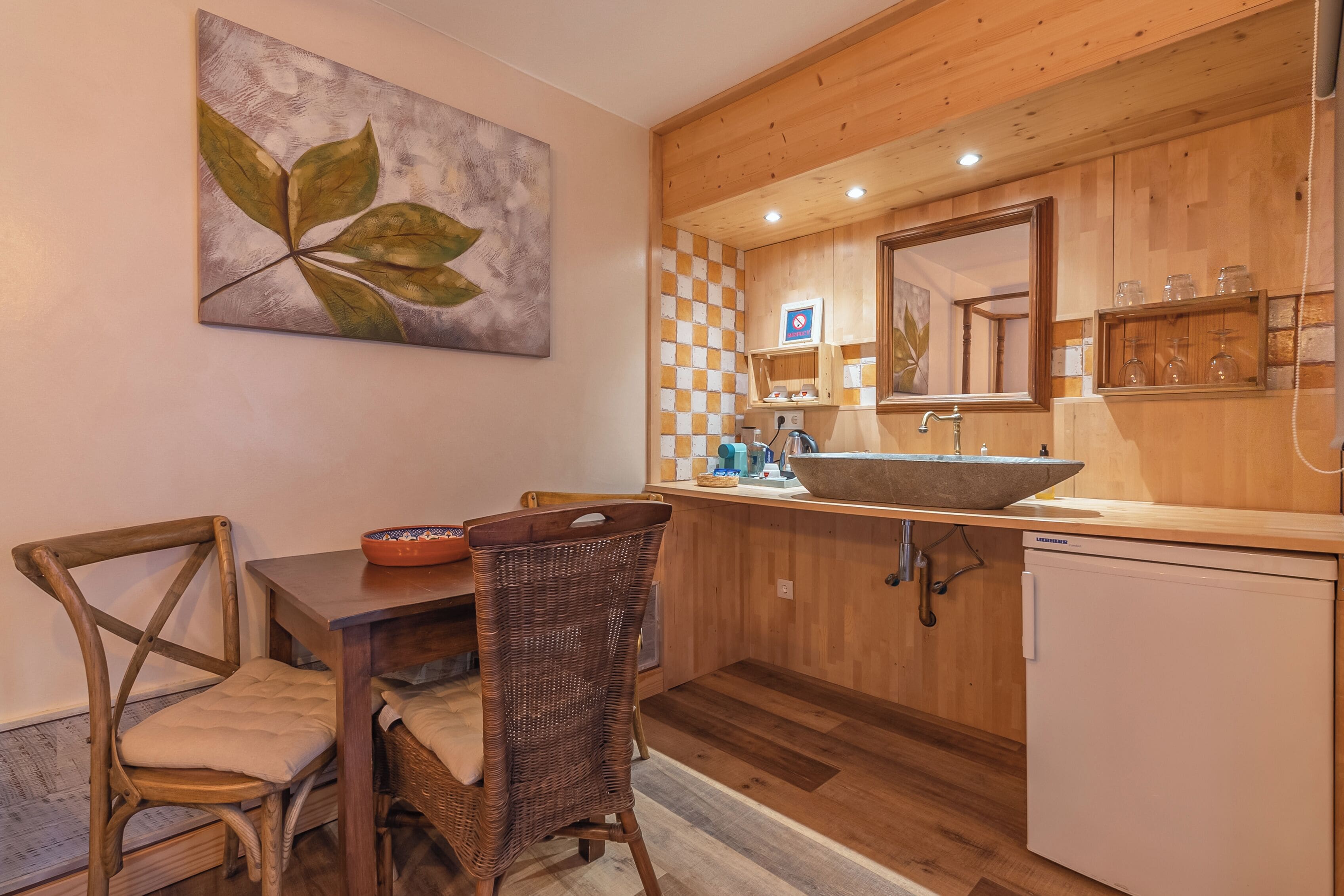 Une cuisine en bois avec un grand évier, une table à manger avec des chaises et un tableau accroché au mur.