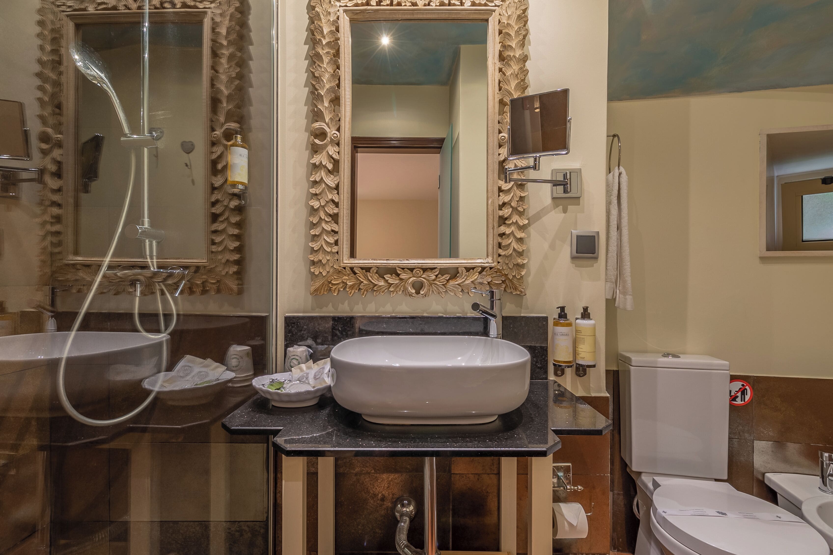 Une salle de bain avec un grand miroir, un lavabo, des toilettes et une douche.