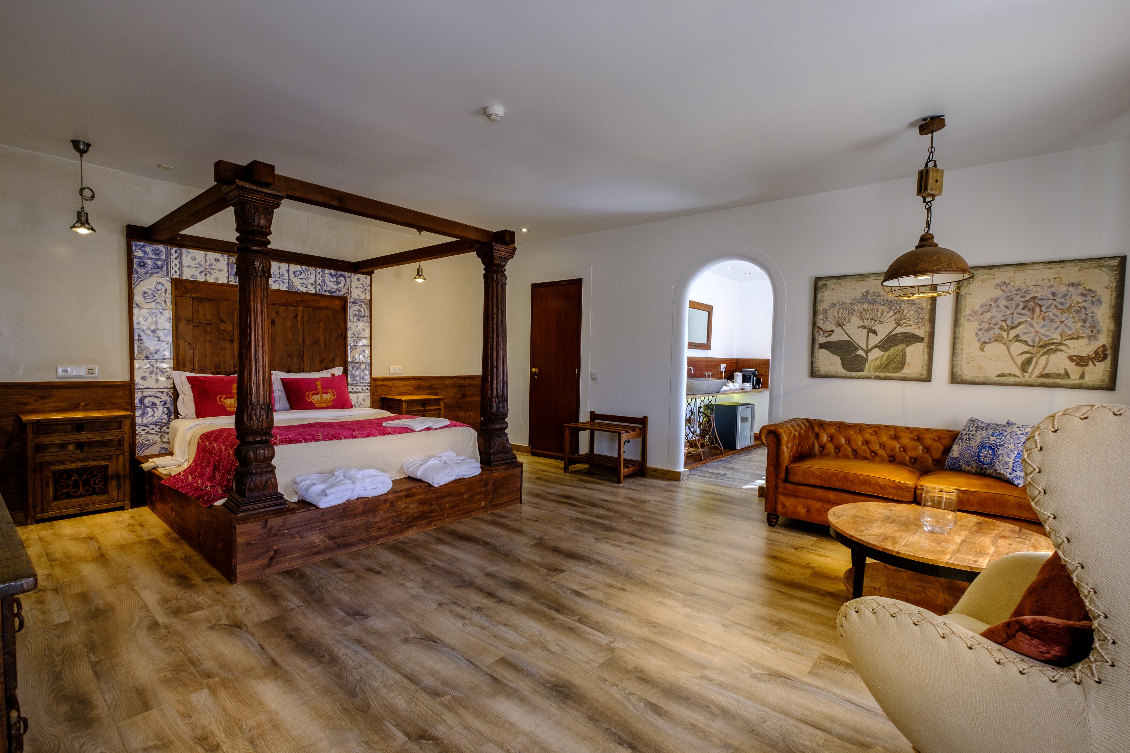 A spacious bedroom with a four-poster bed, a wooden floor, a sofa, and a dining table.