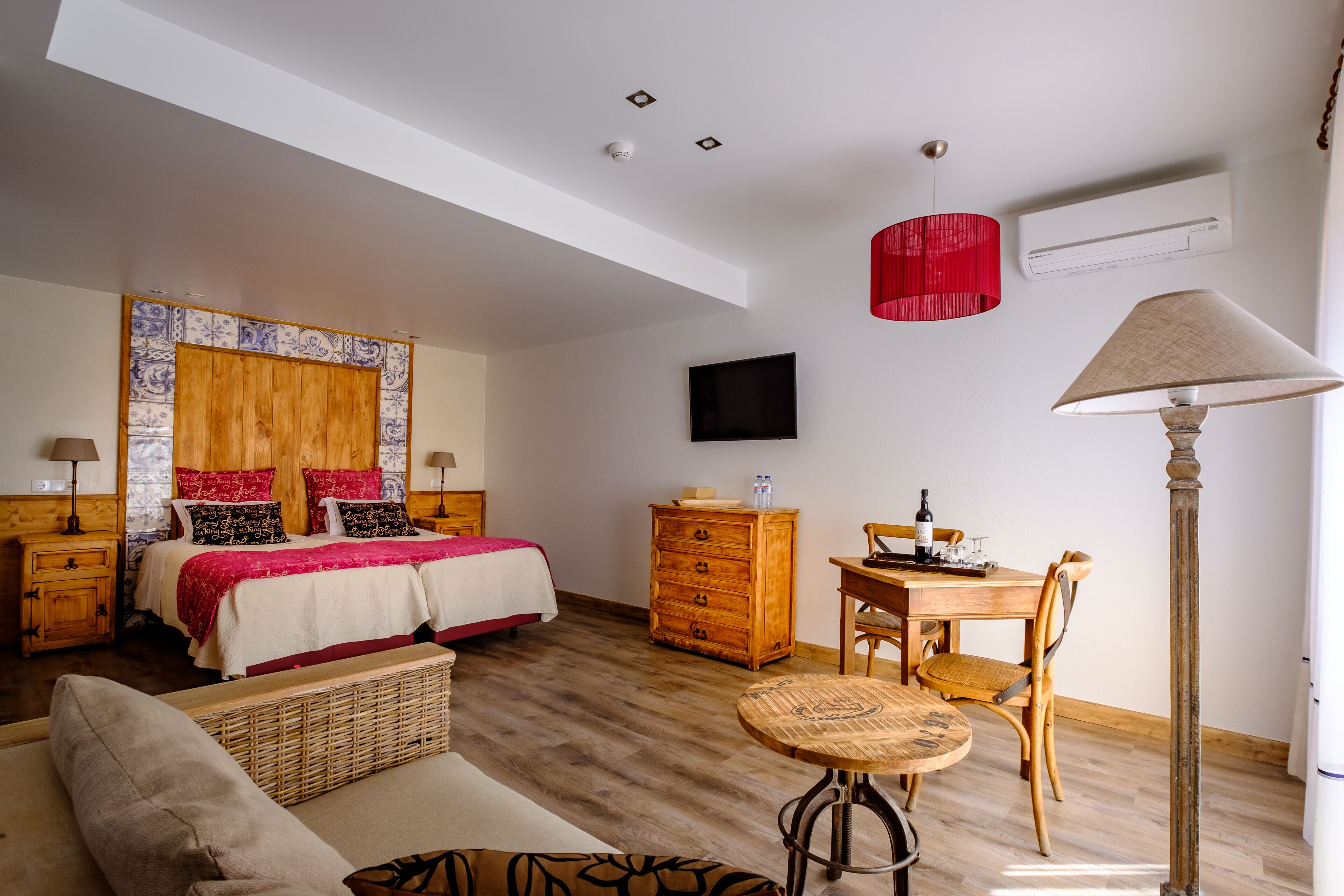 A bedroom with a bed, a wooden dresser, a dining table with chairs, a TV, and a lamp.