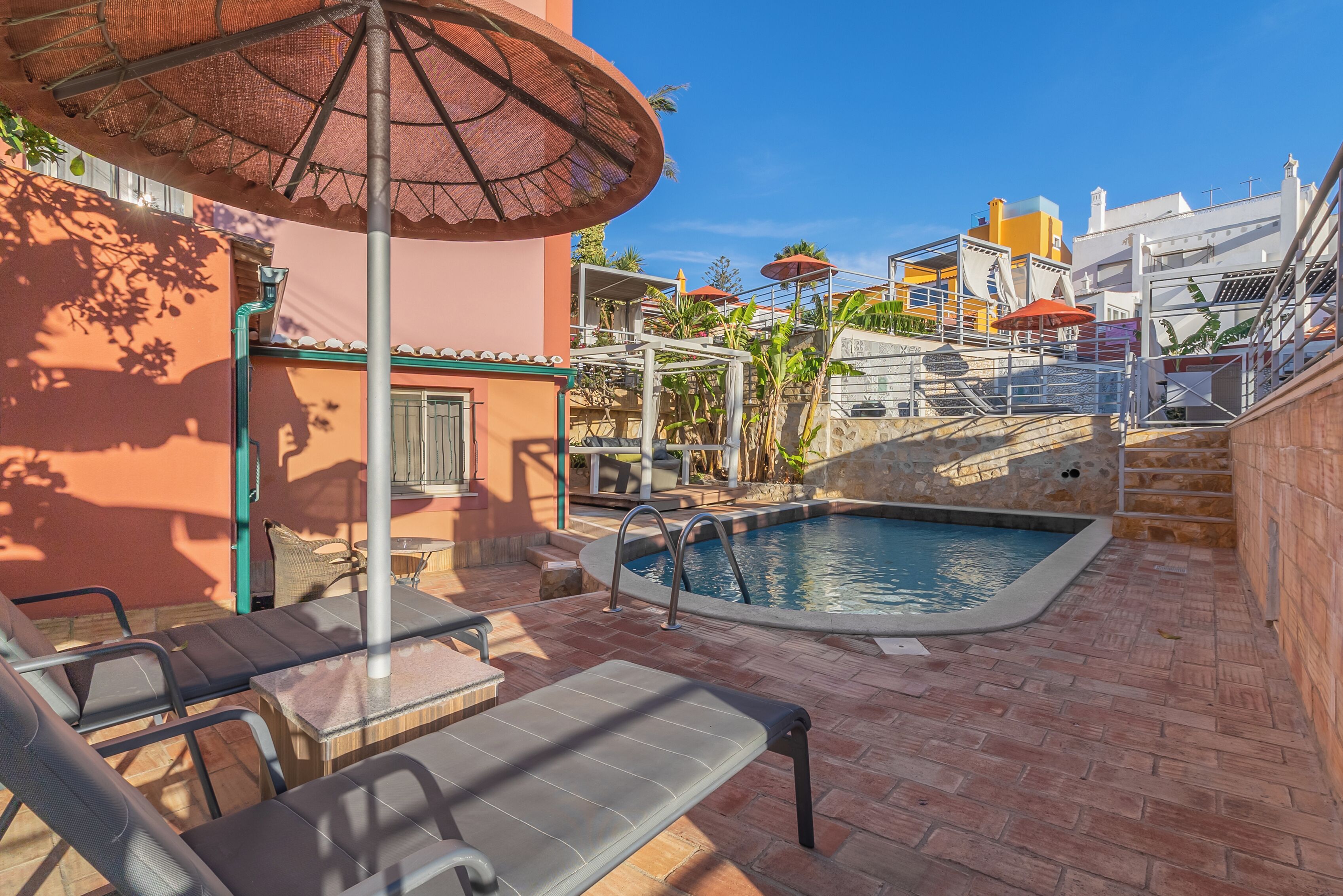Zona de piscina con sillas de descanso, una sombrilla y una escalera que lleva a un edificio.