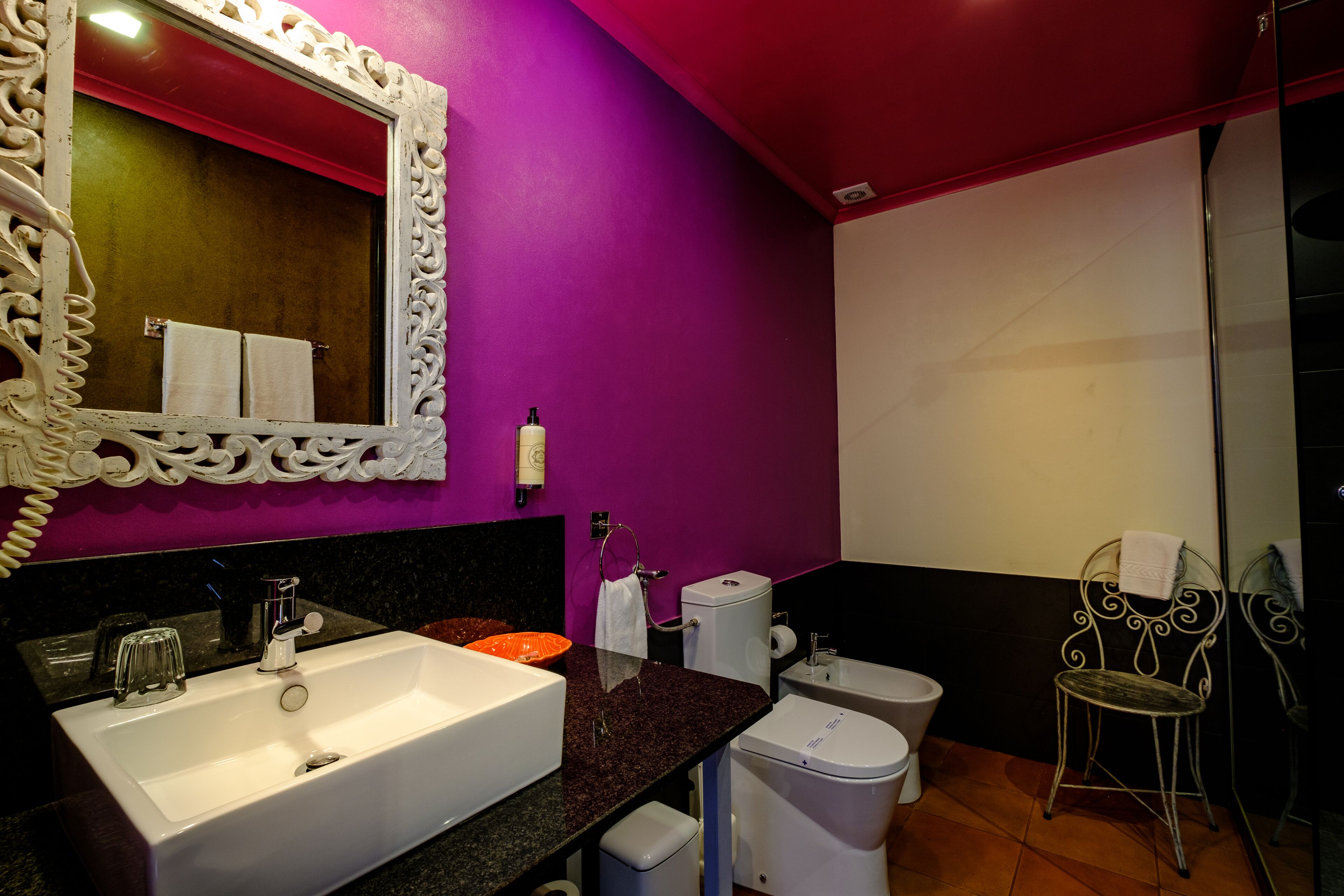 Ein Badezimmer mit einem weißen Waschbecken, einer Toilette und einem Stuhl.