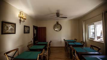 Uma área de refeições com mesas e cadeiras de madeira, um ventilador de teto e um relógio na parede.