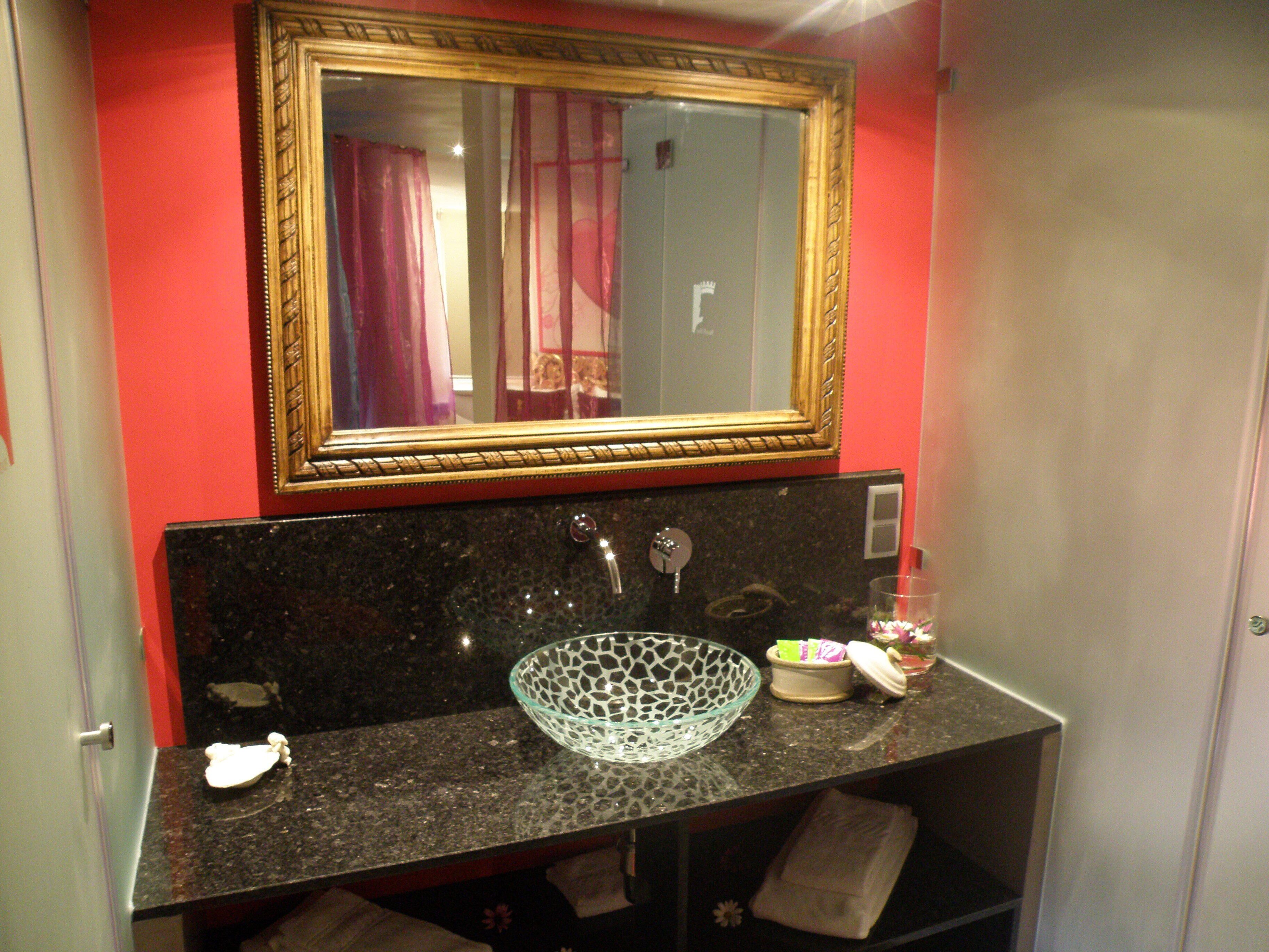A bathroom with a black granite sink, a gold-framed mirror, and a glass bowl on the counter.