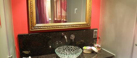 A bathroom with a black granite sink, a gold-framed mirror, and a glass bowl on the counter.