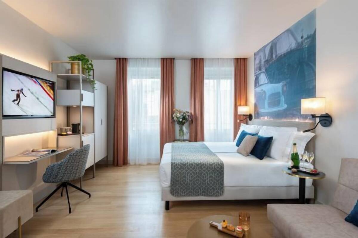 Habitació d'hotel moderna amb llit, escriptori, cadira i televisió penjada a la paret.