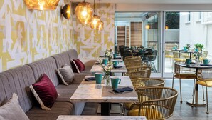 A modern cafe with a long bench seating area, tables with chairs, and hanging pendant lights. - Leonardo Boutique Hotel Rome Termini (Rome)