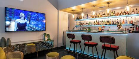 A bar area with a TV, bar stools, and a variety of bottles.