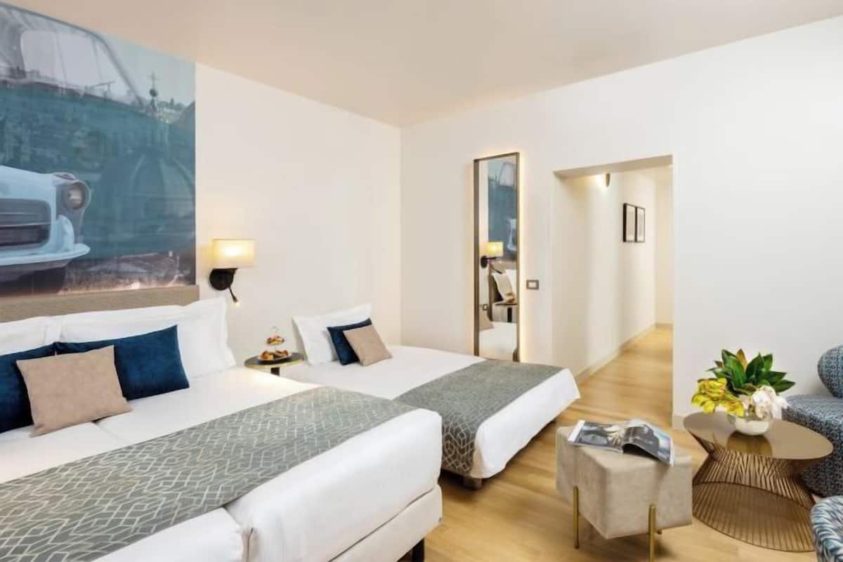 Habitació d'hotel amb dos llits, un sofà, una taula petita i un quadre a la paret.