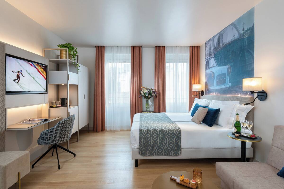 Una habitació d'hotel moderna amb un llit, un escriptori, una cadira, un televisor i un quadre gran a la paret.