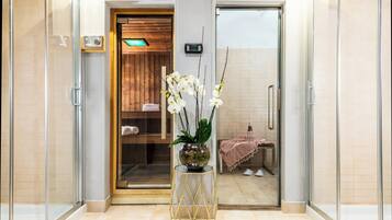 A modern bathroom with a glass shower enclosure, a wooden bench, and a potted orchid plant.