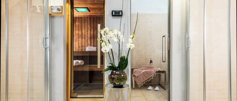 A modern bathroom with a glass shower enclosure, a wooden bench, and a potted orchid plant.