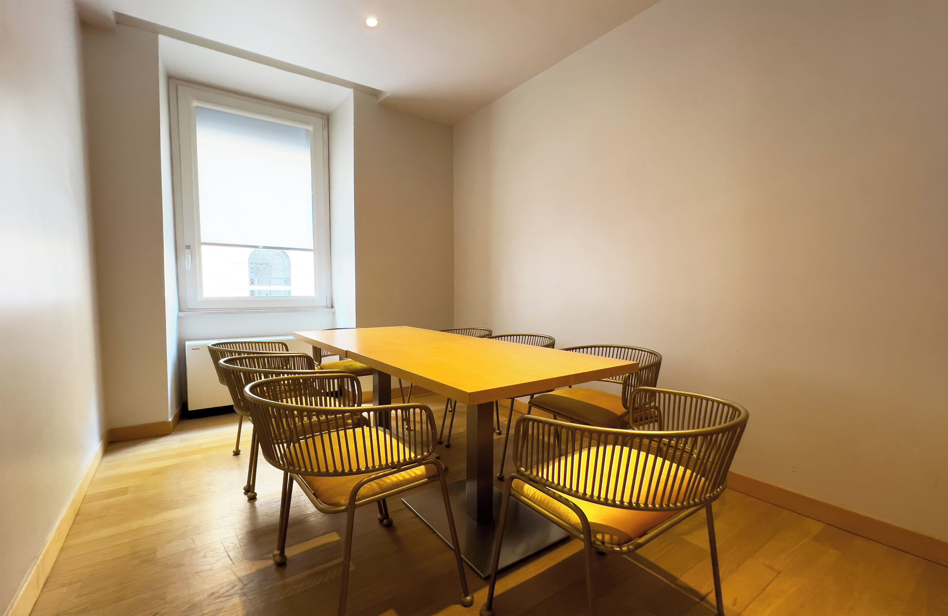 A dining area with a wooden table and six chairs, a window with blinds, and a white ceiling.