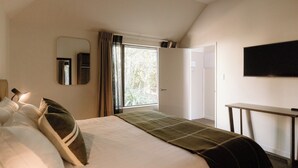 A bedroom with a bed, a mirror, a TV, and a desk.