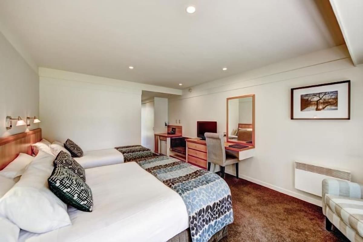 Habitación de hotel con dos camas, un escritorio, una silla, un espejo y un cuadro en la pared.