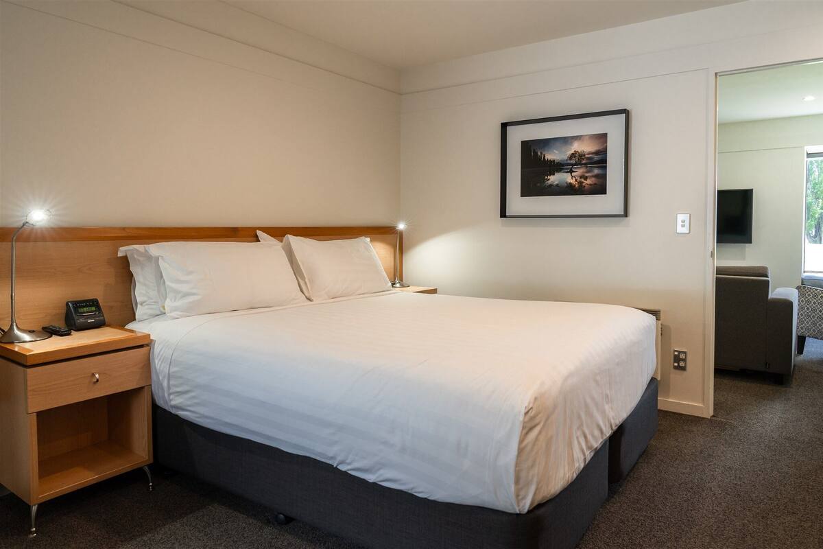 Ein Hotelzimmer mit Bett, Nachttisch, Lampe und einem gerahmten Bild an der Wand.