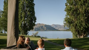 A group of people seated on wicker furniture facing a lake with mountains in the background.