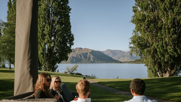 A group of people seated on wicker furniture facing a lake with mountains in the background. - Edgewater (Wanaka)