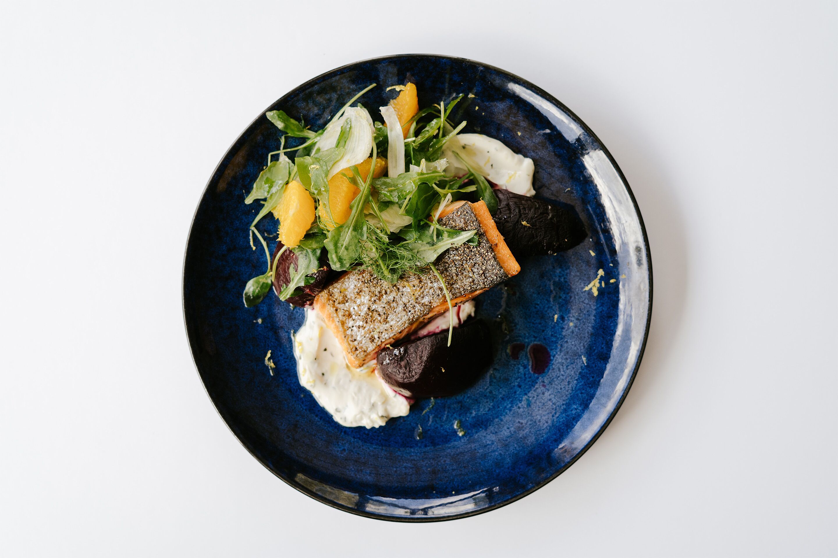 A blue plate with a piece of salmon, greens, and orange segments.