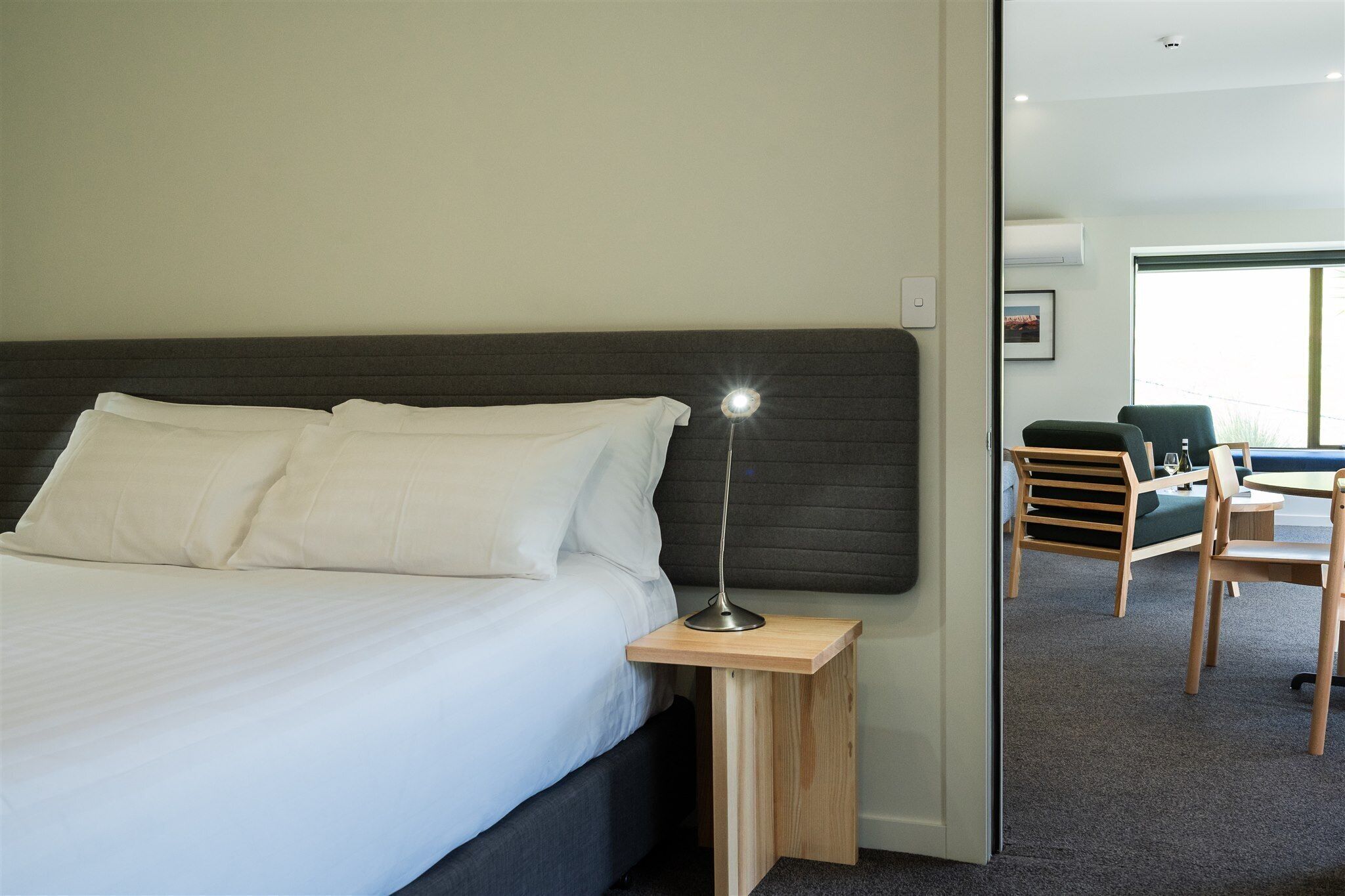 A neatly made bed with white linens, a bedside lamp, and a small wooden nightstand.