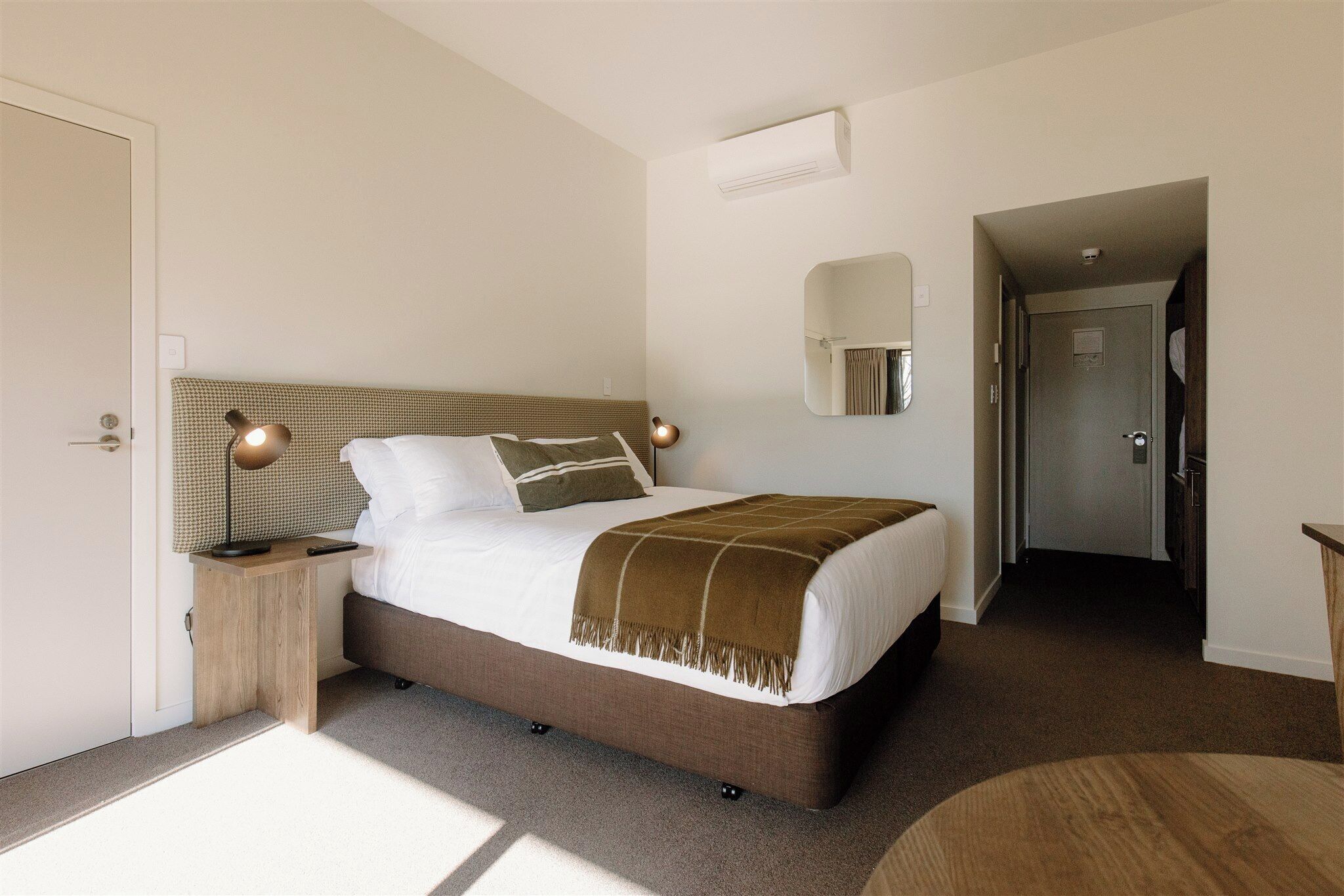 A bedroom with a bed, bedside table, lamp, and a mirror on the wall.