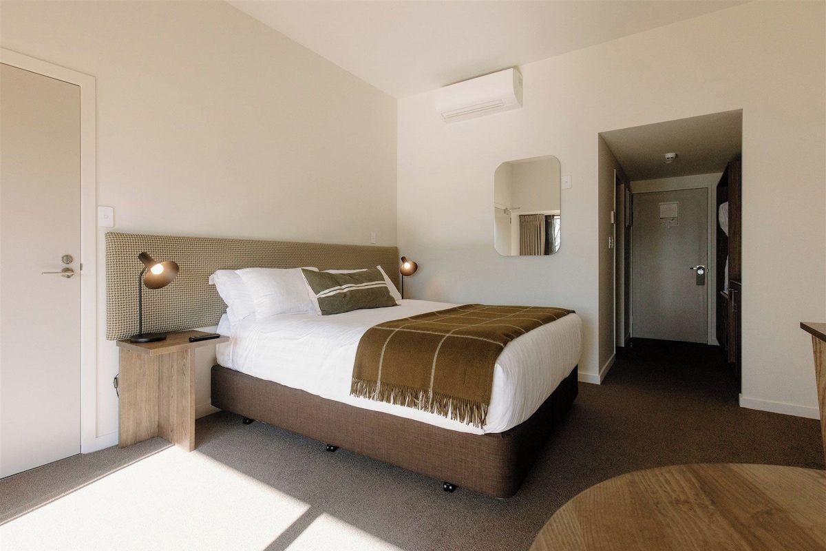 A hotel room with a bed, bedside tables, a mirror, and a door leading to another room.