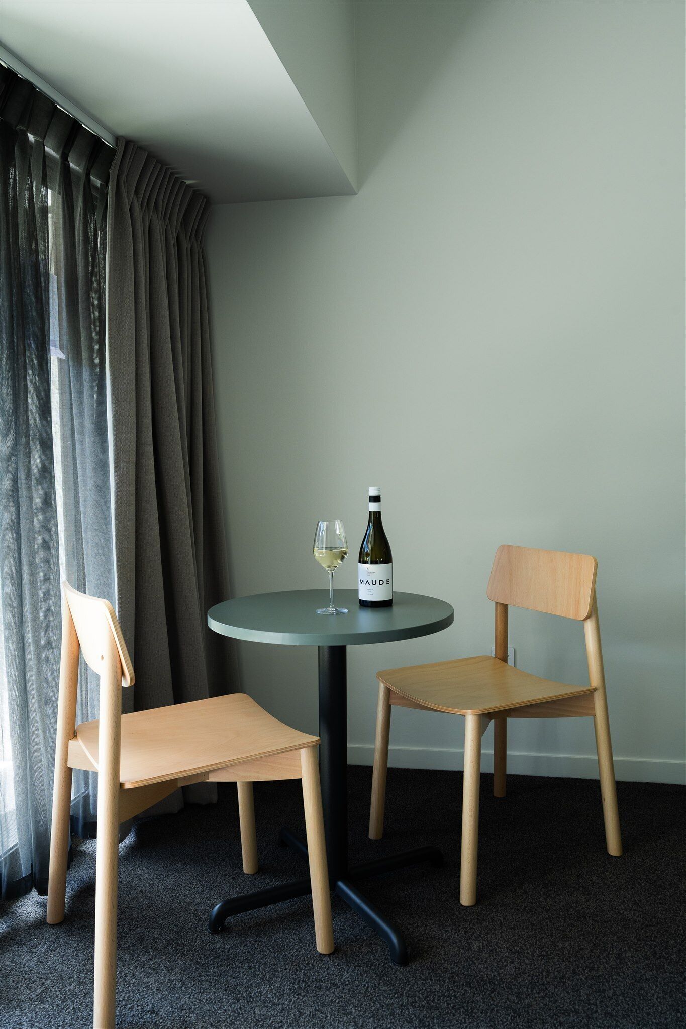 Una habitación con una mesa redonda, dos sillas de madera, una botella de vino y una copa sobre la mesa.