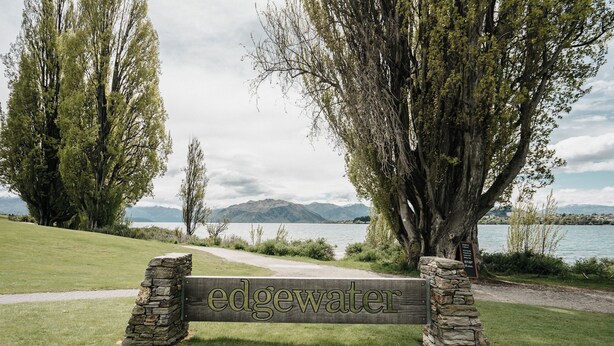A wooden bench with 'edgewater' engraved on it, surrounded by trees and a lake view.