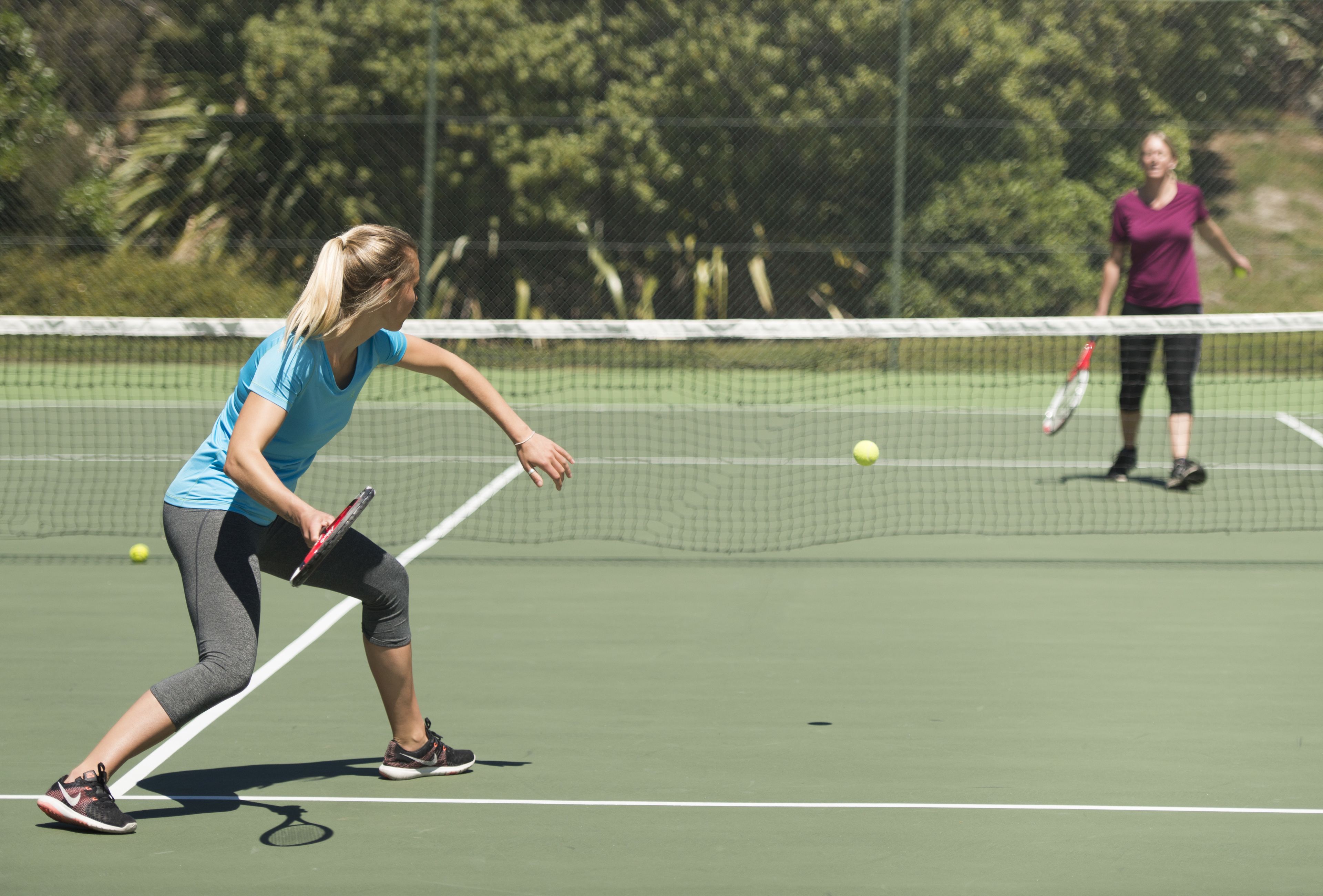 A tennis court with a net in the middle, surrounded by a fence.