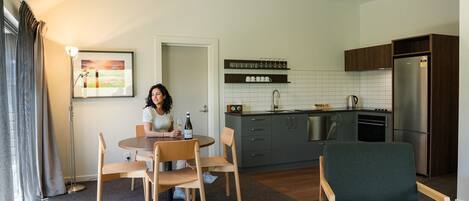 A modern kitchen with grey cabinets, a stainless steel refrigerator, and a dining area with wooden chairs and a table.