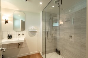 A modern bathroom with a glass-enclosed shower, a white sink with a mirror above, and a small shelf with toiletries.