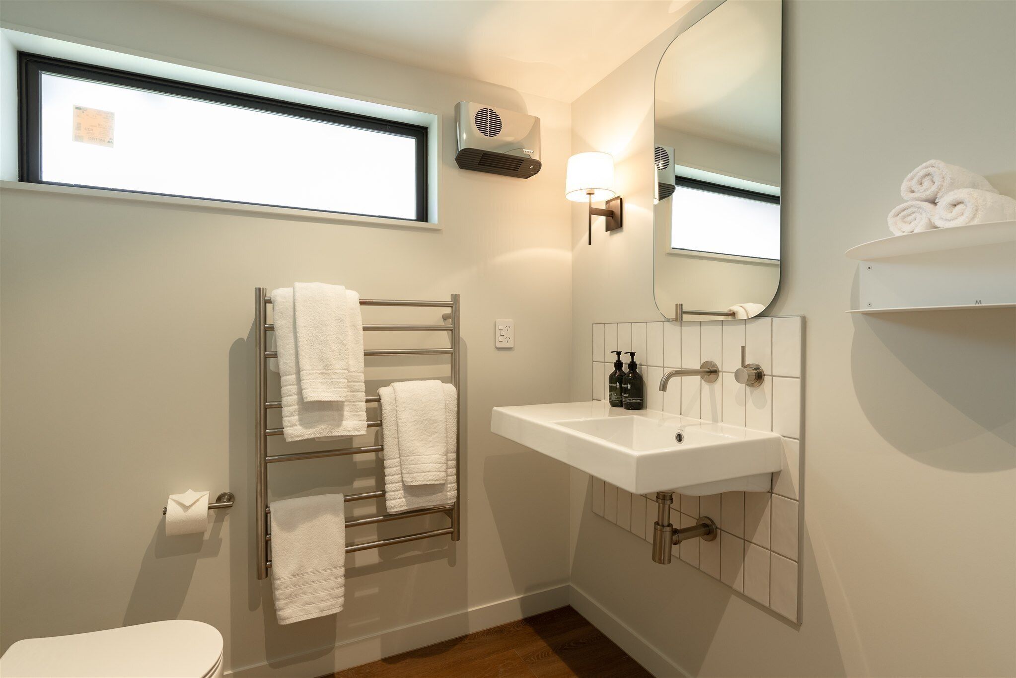 A modern bathroom with a toilet, towel rack, sink, and mirror.